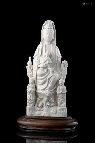 A blanc de chine seated Guanyin, holding a baby and accompanied by two acolytes, wood base (defects) China, 19th century Provenance Milanese private collection Gianni Russo Antiquities (h. 37.5 cm.)...