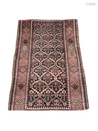 A Kurdish rug, the charcoal compartment field filled with stylised plants, within a madder