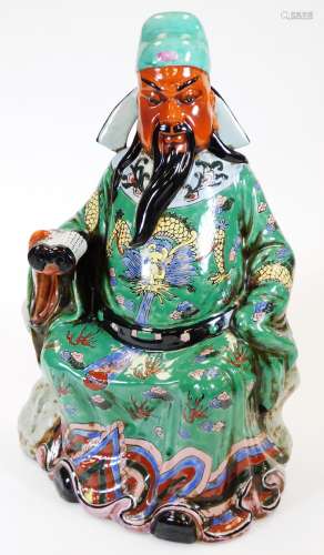 A Chinese porcelain figure of an emperor or immortal, holding a scroll, decorated in yellow,