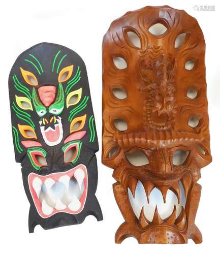 Two various hardwood wall masks, to include one profusely decorated on a black ground, 65cm high. (