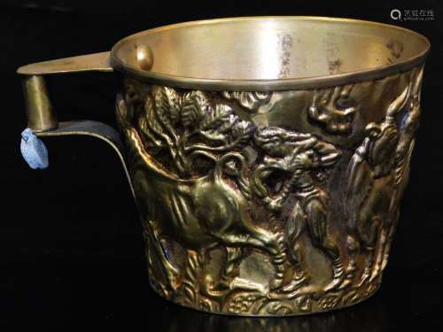A 20thC gilt coloured cup, with compressed cylindrical handle, repousse decorated with buffalo and