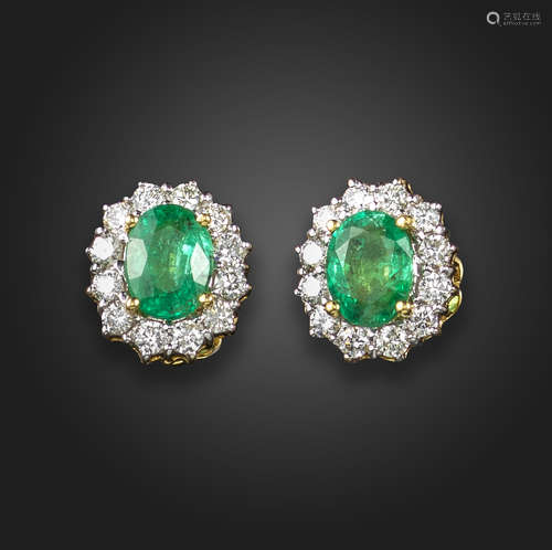 A pair of emerald and diamond cluster earrings, each centred with an oval-shaped emerald within a