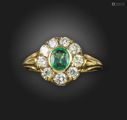 An emerald and diamond cluster ring, the oval-shaped emerald is set within a surround of round