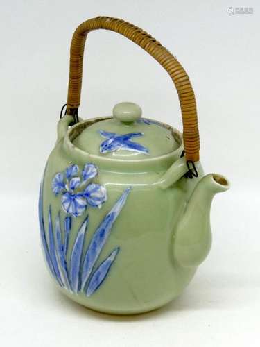 CHINA Porcelain teapot decorated with flowers in relief on a green enamel background. The handle is made of rattan. Ht: 17cm