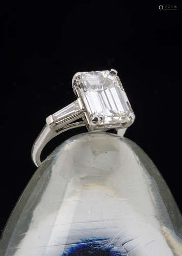 A fine certificated diamond three stone ring, the large emerald cut diamond in four claws flanked by
