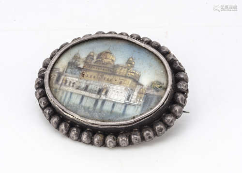 A 19th Century Indian miniature brooch, depicting a palace set within a lake, in white metal frame