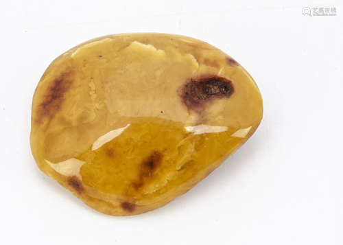 An amber pebble brooch, of natural curved ovoid form, in butterscotch and base metal applied pin,