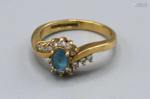 A 9ct Yellow Gold Diamond Set Ring with Central Blue Stone surround by diamonds in a crossover