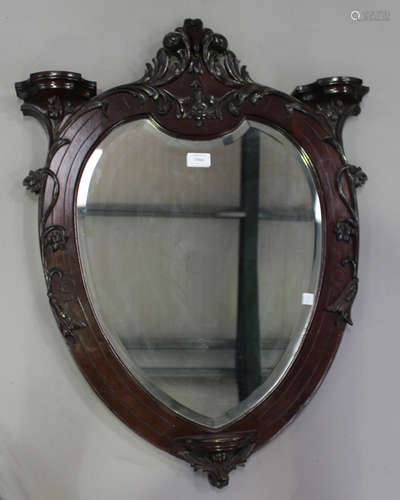 An Edwardian mahogany wall mirror of cartouche form, the foliate carved frame with three small