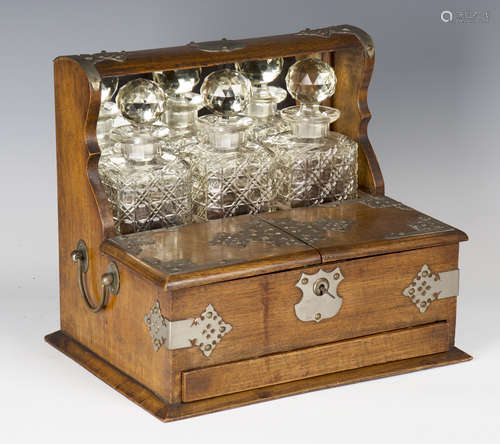 An Edwardian oak and plate mounted three-bottle tantalus, the double-hinged compartment above a