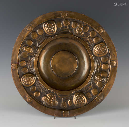 An early 20th century Arts and Crafts pressed copper charger, the border decorated in relief with