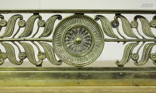 A Regency cast brass fender with central rosette flanked by curled laurel leaves and flowerheads,