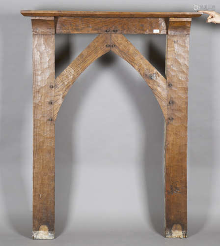 An early 20th century Arts and Crafts oak fire surround, the arched frame with pegged joints and