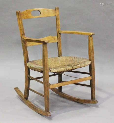 An early 20th century Arts and Crafts beech framed rocking armchair with a rush seat, height 80cm,