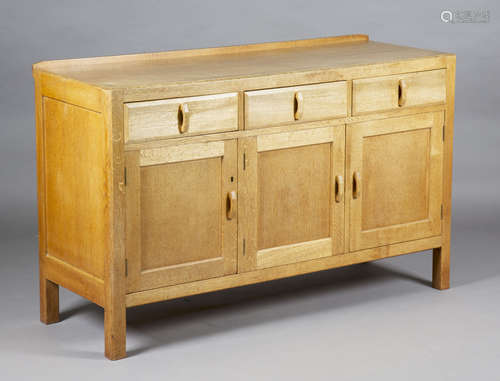 An early 20th century Heals pale oak sideboard, fitted with three drawers above panelled cupboard