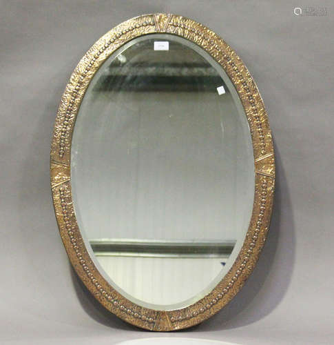 An early 20th century Arts and Crafts oval copper wall mirror with hammered decoration, 85cm x