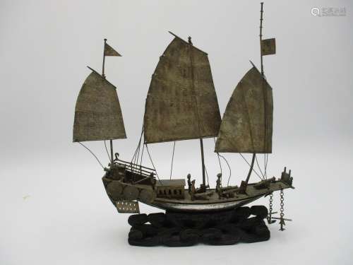 A Chinese white metal model of a junk ship, supported on a carved and pierced hardwood base