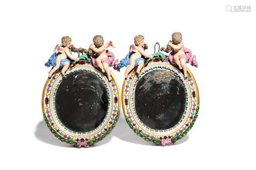 A pair of Meissen mirrors 19th century, of oval form, each surmounted with two winged putti