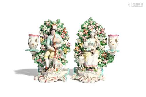 A pair of Derby figures of musical shepherds c.1760, each modelled seated before flowering bocage,