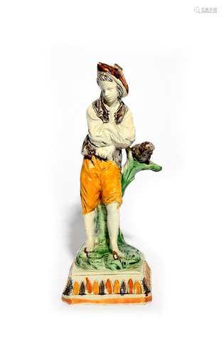 A Pratt ware figure of a young boy c.1800-10, standing with arms folded and leaning against a branch