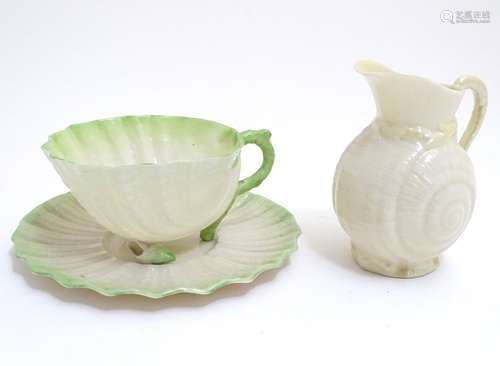 A Belleek tea cup and saucer of shell form with green highlights. Together with a Belleek jug, the