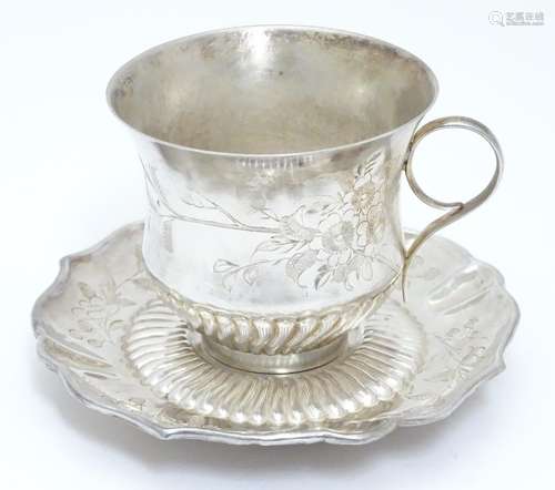 Chinese Export : An Oriental white metal teacup and saucer with engraved floral and bird