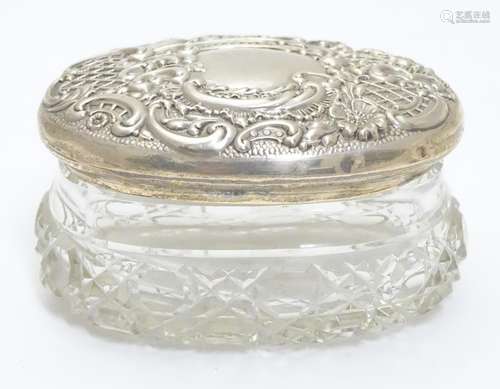 A cut glass dressing table pot of oval form with silver top having embossed decoration. Hallmarked