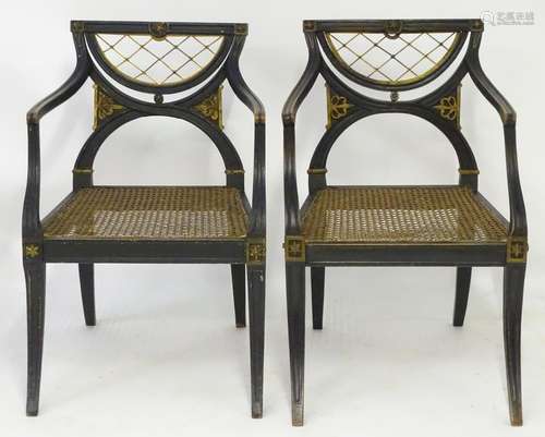 A pair of ebonised Regency open armchairs with gilt and brass detailing above a caned seat, the