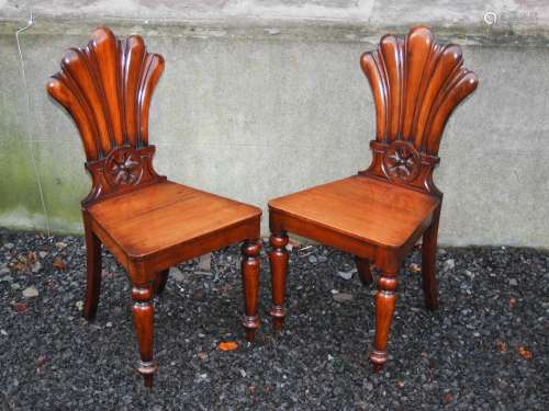 A pair of 19th century mahogany fan back hall chairs, the fan shaped backs carved with floral