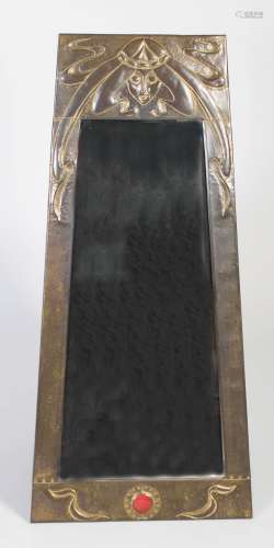 An Arts & Crafts brass wall mirror, the tapered embossed frame decorated with the stylised head of a