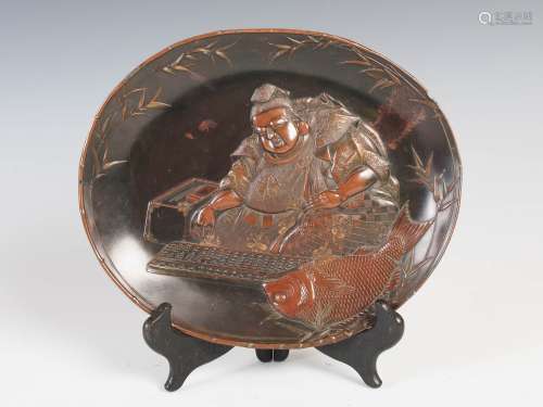 A Japanese bronzed spelter dish, Meiji Period, decorated in relief with seated figure with