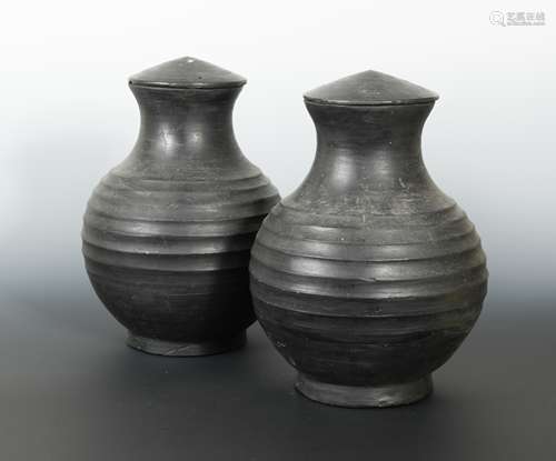 A pair of Chinese burnished pottery lidded vases, with deeply ribbed bodies, perhaps Han Dynasty,