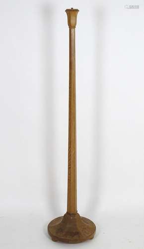 An early 20thC Heals oak standard lamp with a tapering stem and shaped base, raised on three small