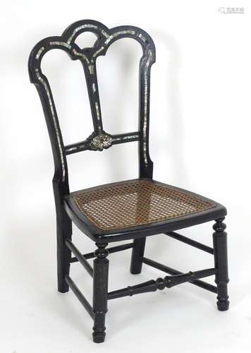 An early 20thC ebonised childs chair with mother of pearl decoration and a caned seat. 15