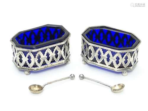 A pair of silver salts with pierced decoration and blue glass liners, raised on four ball feet.