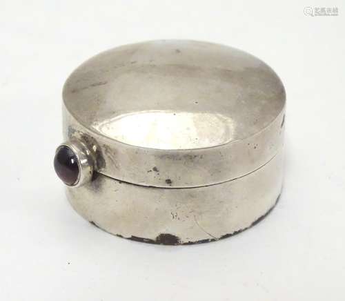 A circular silver pill box with garnet coloured cabochon opener. Bears import hallmarks for