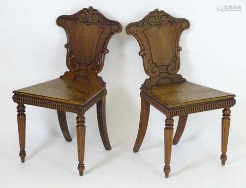 A pair of Victorian oak hall chairs with shaped and carved backrests above gadrooned front rails and