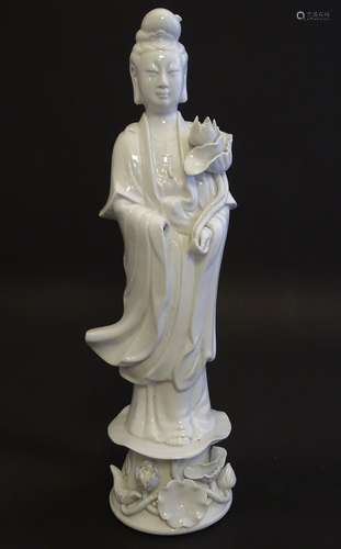 A Chinese blanc de chine figure of Guanyin standing holding flowers, raised on a base of lotus