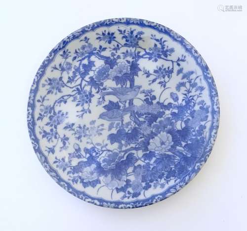 An Oriental blue and white plate with floral and foliate detail with birds on branches. The