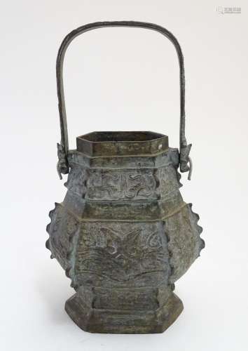 An Oriental cast baluster vase of hexagonal form with a swing handle, the body decorated with panels