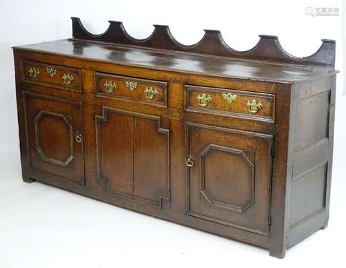 An 18thC oak dresser base with a shaped upstand above three short drawers with brass back plates and