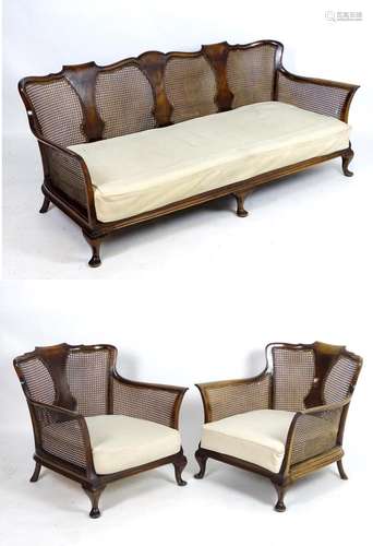 An early / mid 20thC bergere suite, comprising a sofa and two armchairs, having figured and shaped