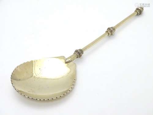 An unusual silver gilt serving spoon, the bowl having rounded serrated edge, the stem and terminal