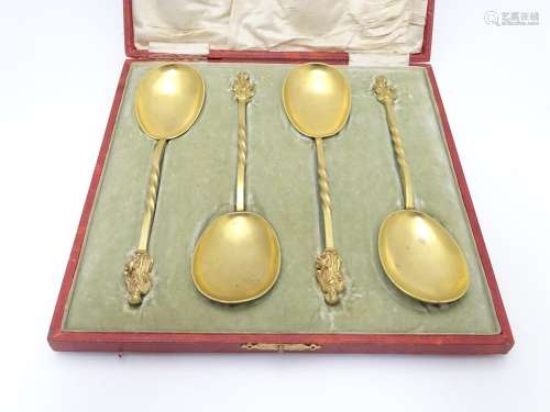 A cased set of four gilded serving spoons surmounted by a religious figure. Each approx. 8
