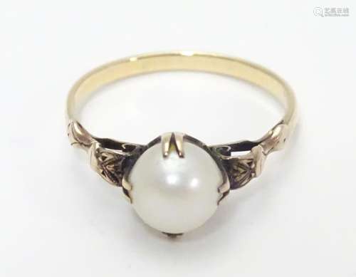 A yellow metal ring with claw set pearl and decorative shoulders. Ring size approx O Please Note -
