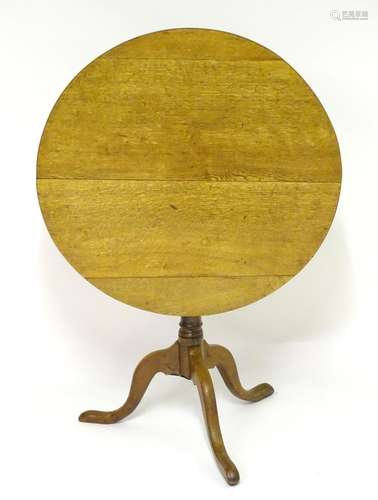 A 19thC oak tilt top table with a circular top above a turned pedestal tripod base with three