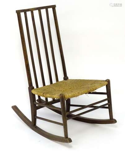 An early 20thC Arts & Crafts style rocking chair with a shaped top rail and spindled backrest