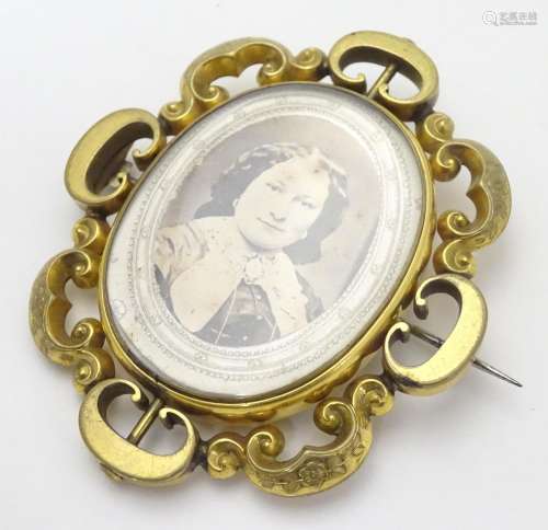 A Victorian gilt metal brooch of locket form with glazed font and back central section within a C-