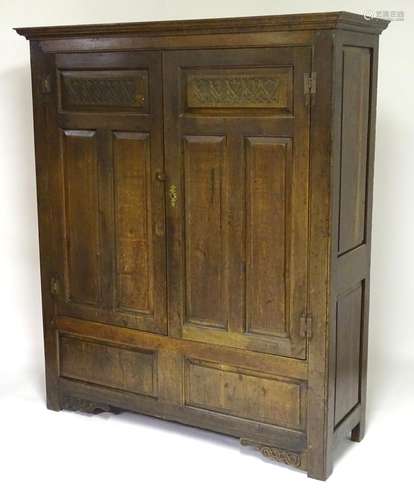 An early 20thC oak wardrobe with a moulded cornice above two doors supported by H-bracket hinges,