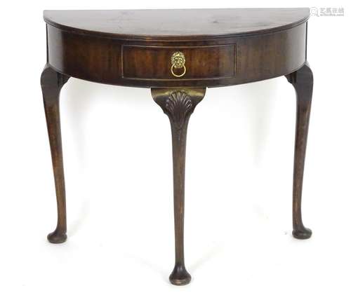 An early 20thC demi lune hall table raised on three cabriole legs with carved knees and pad feet.